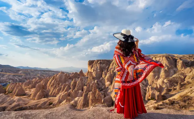 Visitor in traditional dress overlooking Cappadocia Red Valley fairy chimneys at golden hour during a Turkey Family Tour