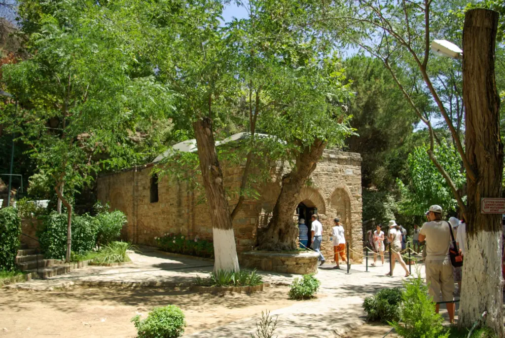 Stone chapel of the House of the Virgin Mary near Ephesus under tall shade trees on a summer day