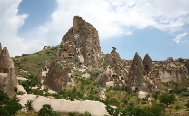 Uçhisar Castle rising above fairy chimneys and cave dwellings in Cappadocia, viewed from the valley below.