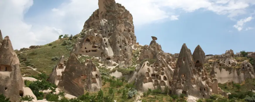 Uçhisar Castle rising above fairy chimneys and cave dwellings in Cappadocia, viewed from the valley below.